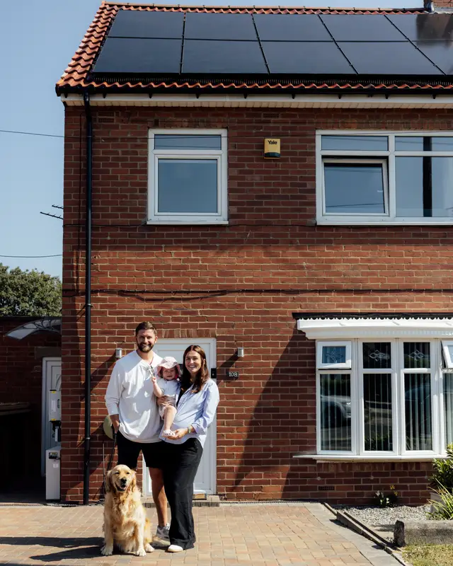 Family and their golden retriever outside their brick semi with new black solar panels on the roof and battery units on the side wall