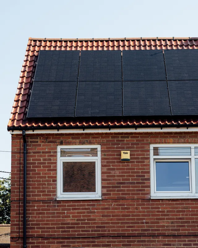 Full-black solar panels covering the roof of a red-brick semi-detached house