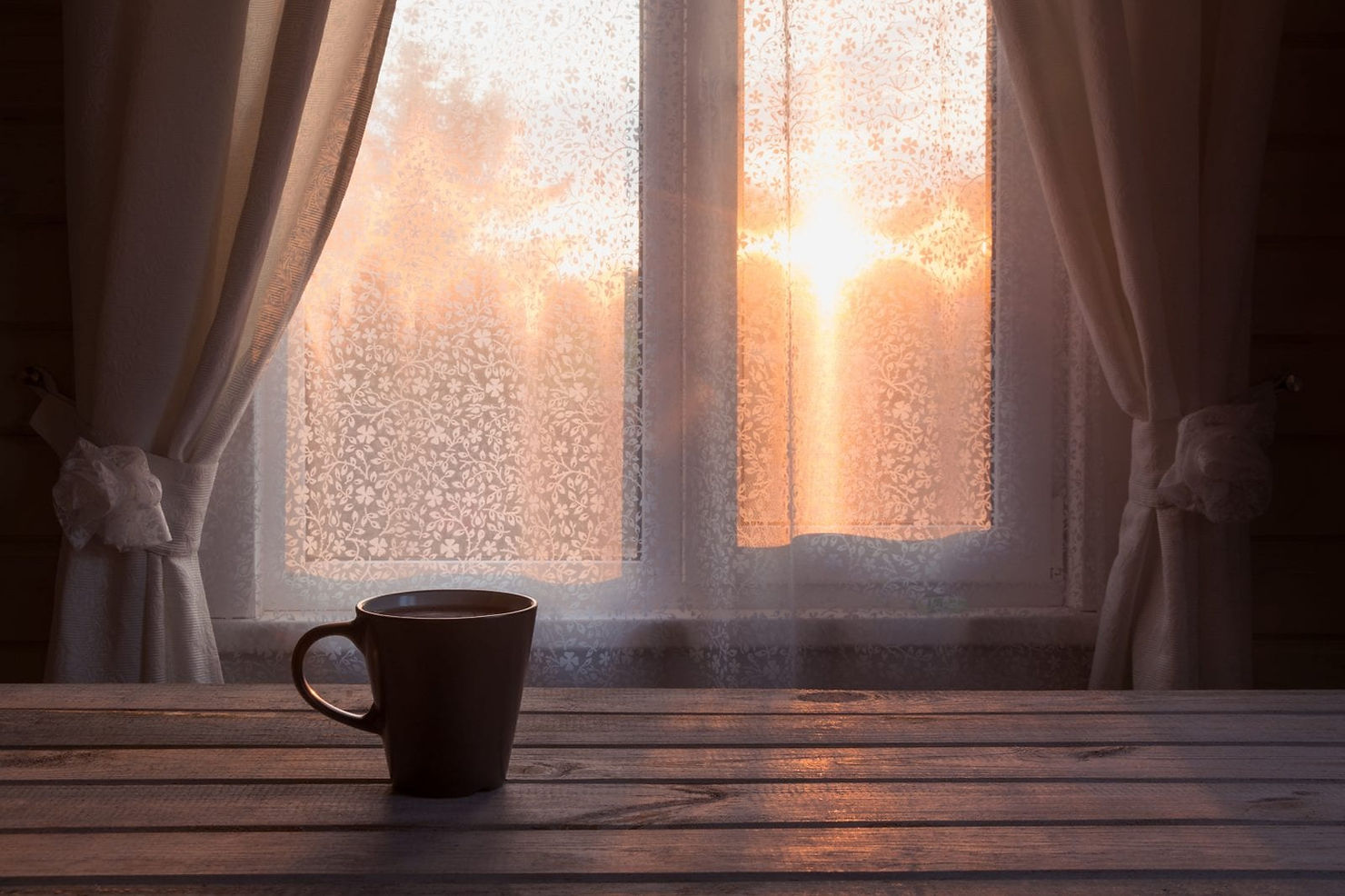 Cup of coffee by a window at sunrise